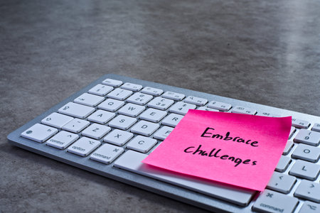 Embrace challenges sticky note left on keyboard. The bright note stands out against the keys,...
