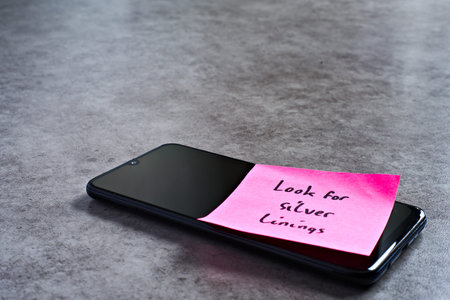 Look for silver linings sticky note left on smartphone. The bright note stands out against the keys,...