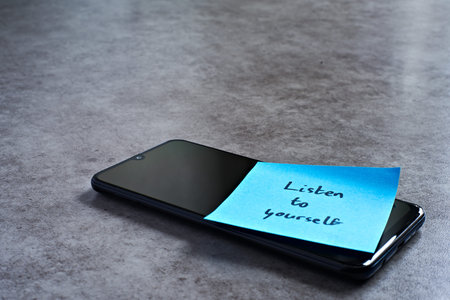 Listen to yourself sticky note left on smartphone. The bright note stands out against the keys,...