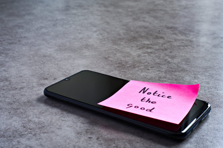 Notice the good sticky note left on smartphone. The bright note stands out against the keys,...