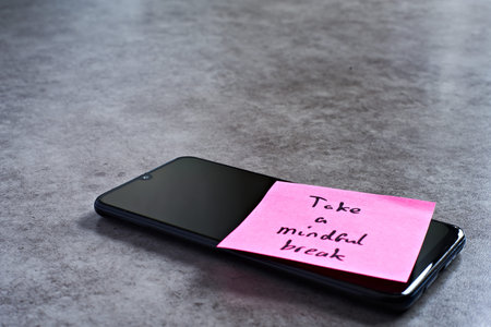 Take a mindful break sticky note left on smartphone. The bright note stands out against the keys,...