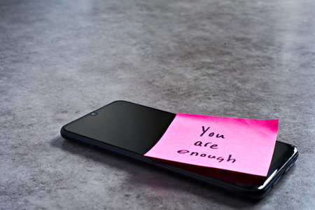 You are enough sticky note left on smartphone. The bright note stands out against the keys,...