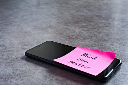 Mind over matter sticky note left on smartphone. The bright note stands out against the keys,...