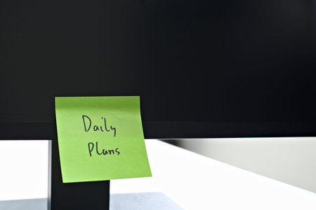 Daily Plans sticky note left on a monitor. The bright note stands out against the monitor,...