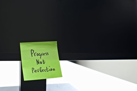 Progress Not Perfection sticky note left on a monitor. The bright note stands out against the...