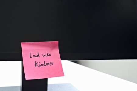 Lead with Kindness sticky note left on a monitor. The bright note stands out against the monitor,...