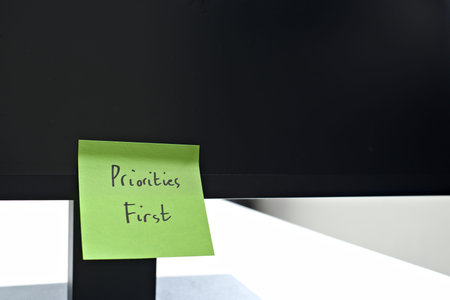 Priorities First sticky note left on a monitor. The bright note stands out against the monitor,...