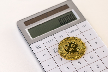 Golden bitcoin on white calculator and cream tableの写真素材