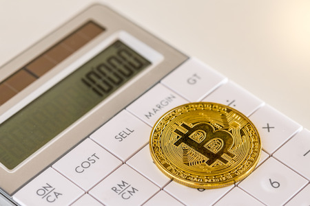 Golden bitcoin on white calculator close-up imageの写真素材