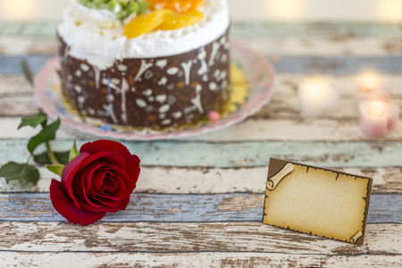 Empty greeting card, single red rose, and birthday cake on turquoise tableの写真素材