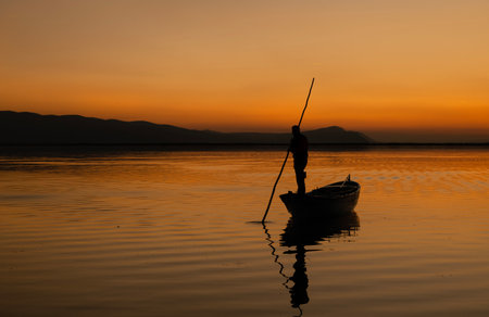 Sunset in Denizli Civril illuminated lake is approaching the shore with a fishing boatの写真素材