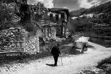 Old woman walking in a village in the mountains. Black and white photo.