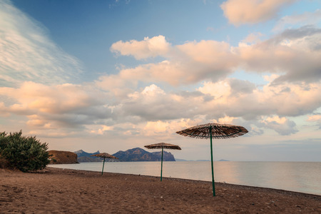 Seascape view of the sandy beach with three umbrellas and cloudy skyの写真素材