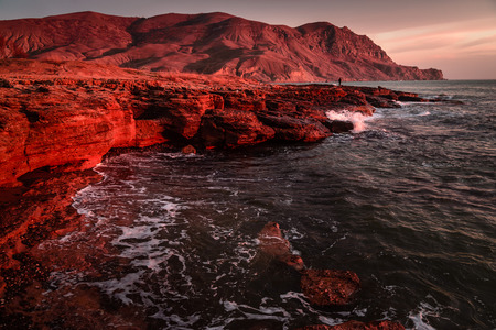 Storm sea at sunset on the mountain coast in red toneの写真素材