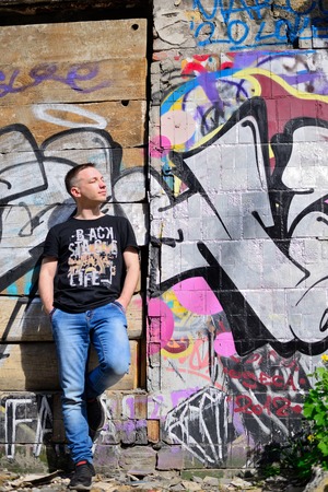 Young man leaning on wall with graffiti. Screwing up his eyes.の写真素材