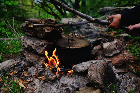 Man holds a kettle over a fire, cooking a meal in a terpohod, hands in a frameの写真素材