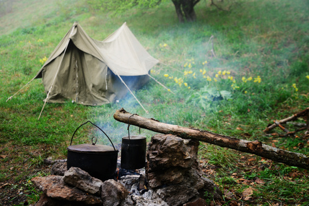 Two bowlers at the stake, cooking in the tourist camp, a tent on the backgroundの写真素材