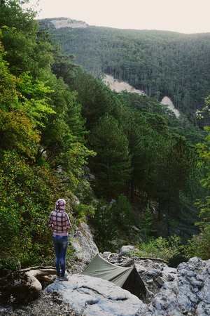 traveler girl woman adventurer standing and looking at the forest on the edge of a cliffの写真素材