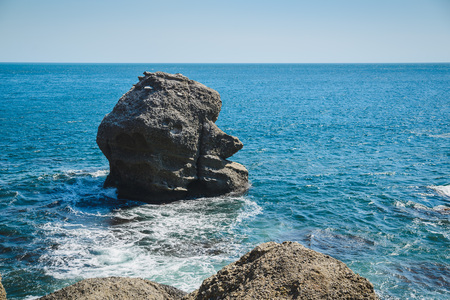 Large stone in the shape of a head in a wavy blue seaの写真素材