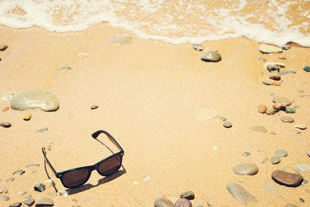 Sunglasses on a sandy beach with sea wave on a sunny summer day with copy spaceの写真素材