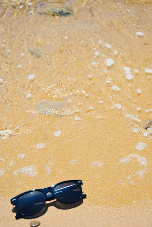 Sunglasses on a sandy beach with sea wave on a sunny summer day with copy spaceの写真素材