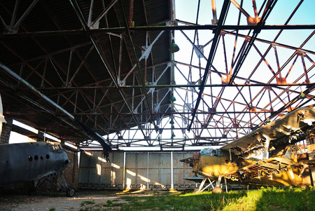 Old retro broken airplane in an abandoned destroyed hangar in the setting sunの写真素材
