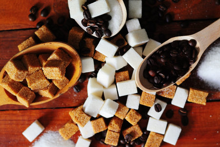 Grains of coffee and white and brown cane sugar in spoons on a wooden background