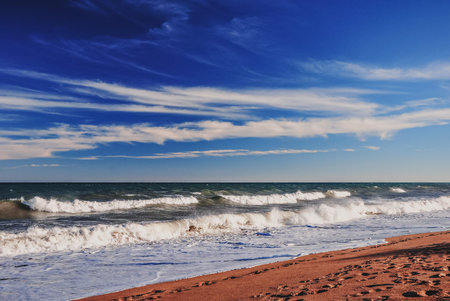 Storm on the sea on a sandy beach against the blue sky with clouds on a bright day