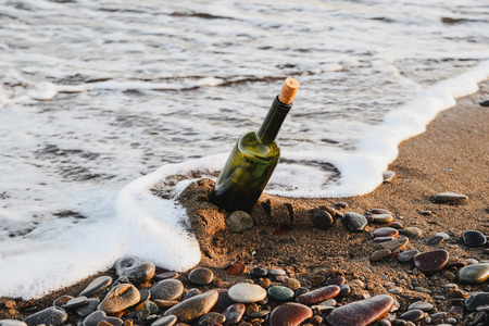 Wine bottle with a cork stopper on a sandy beach by the seaの写真素材