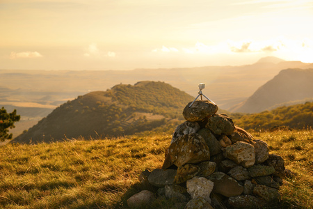 Action camera mounted on a tripod at the top of a mountain on a pile of stones shoots a golden sunsetの写真素材
