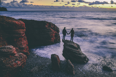 Couple admiring the sunset on the sea on a huge stoneの写真素材