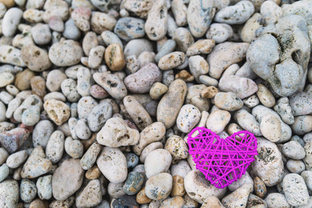 Purple knitted heart on a rocky beach coast, romantic background, space for text