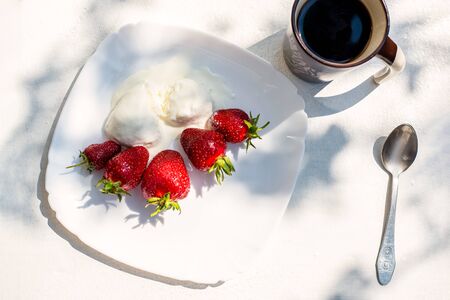 Ripe fresh strawberries and ice cream on a plate on the table, breakfast in the yardの写真素材
