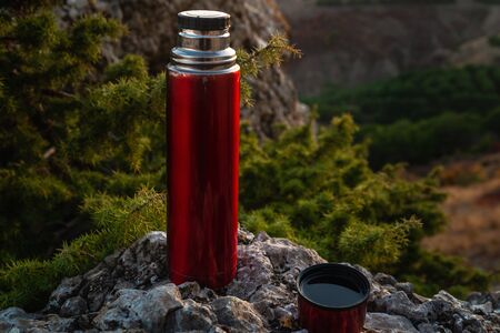 Red bottle with hot tea on a camping trip in the mountainsの写真素材