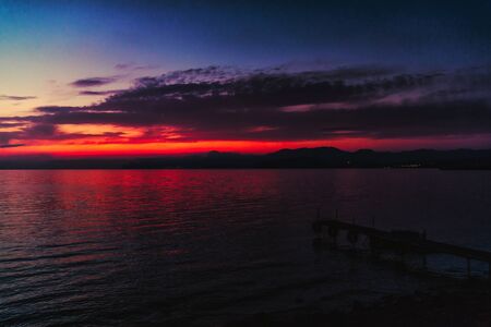 Blue-red sunset over the sea, a small pier for boats on the seashoreの写真素材