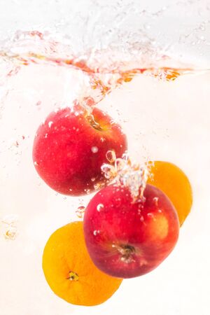 Two red apples and two tangerines with a splash fall into the water in an aquarium on a white backgroundの写真素材