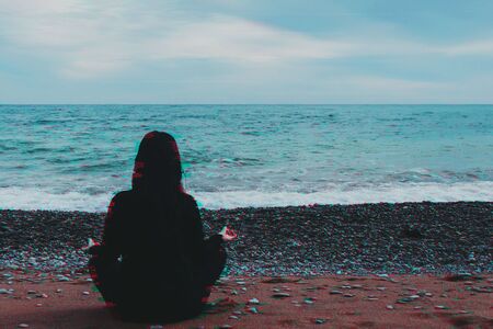 Girl in lotus position doing yoga on the sea beach in glitch effectの写真素材