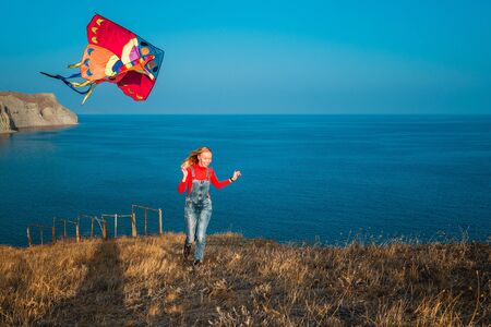 Young girl launches a colorful kite on the sea coastの写真素材