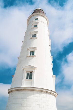 Tall lighthouse tower on a background of blue cloudy skyの写真素材