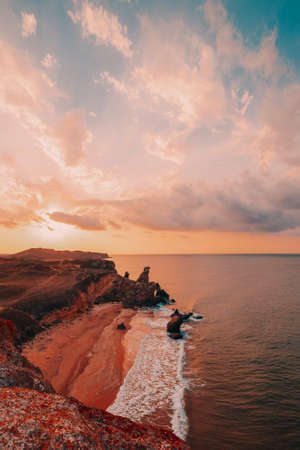 Amazing sunset at sea, beauty of nature. Scenic view of the sea, rocky coastline and sandy beach, golden sky and sun. Copy space on the fantastic sky. Vertical shoot.の写真素材