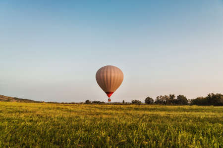 Hot air balloon in clear blue sky low over green gladeの写真素材