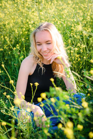 Blonde girl in a black bodysuit with a white hat walks in a rapeseed field, having fun, view from the backの写真素材