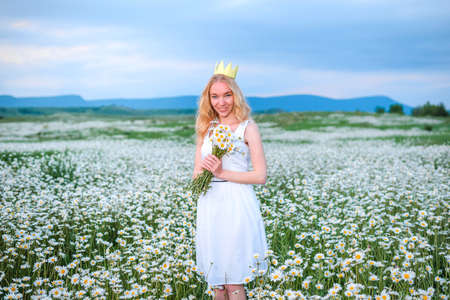 Blonde girl in a black bodysuit with a white hat walks in a rapeseed field, having fun, view from the backの写真素材