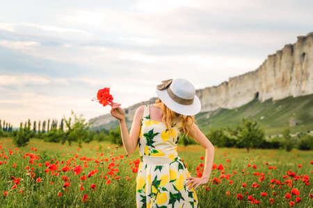 Blonde girl in a black bodysuit with a white hat walks in a rapeseed field, having fun, view from the backの写真素材