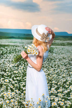 Blonde girl in a black bodysuit with a white hat walks in a rapeseed field, having fun, view from the backの写真素材