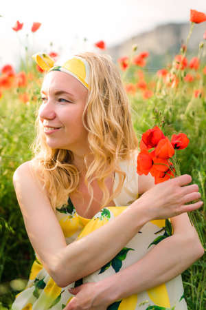 Girl in a hat and dress with a bouquet of poppies in a poppy fieldの写真素材
