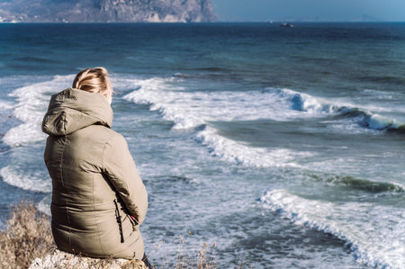 A girl sits on a cliff on the seashore during a storm
