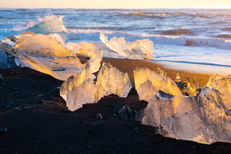 Diamond Beach in Iceland. Icebergs Shining on Black Volcanic Sand at Sunset. Clear Ice Crashed by...