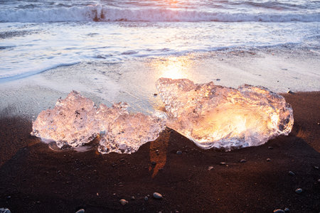 Diamond Beach in Iceland. Icebergs Shining on Black Volcanic Sand at Sunset. Clear Ice Crashed by...