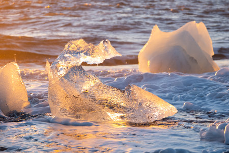 Icebergs Shining on Black Volcanic Sand at Sunset. Clear Ice Crashed by Ocean Waves. Famous Tourist...